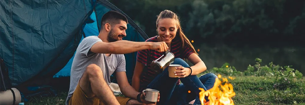 Zwei Personen trinken am Lagerfeuer Kaffee.